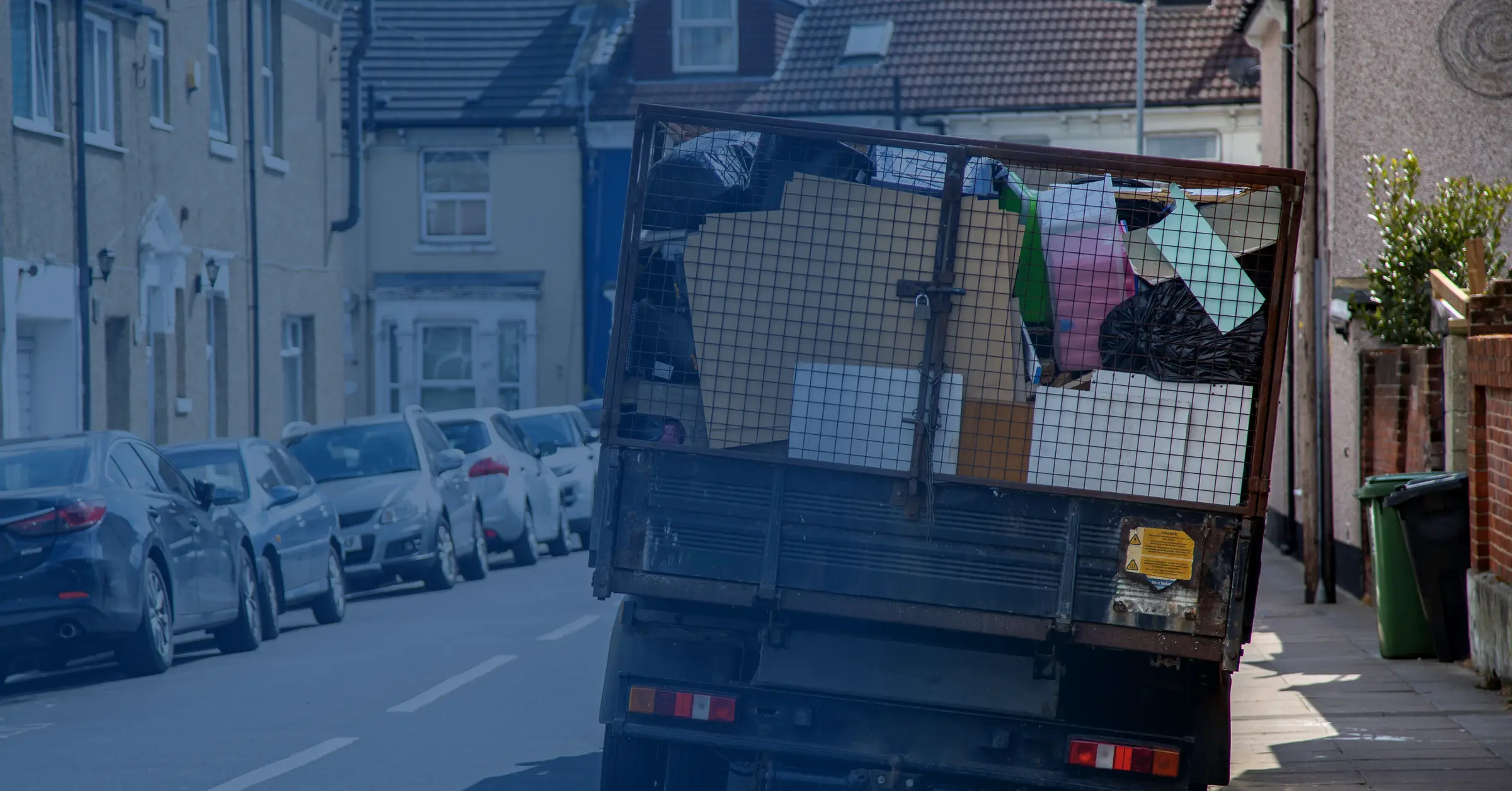 A clearance tipper on a terraced street, its cage loaded with household waste