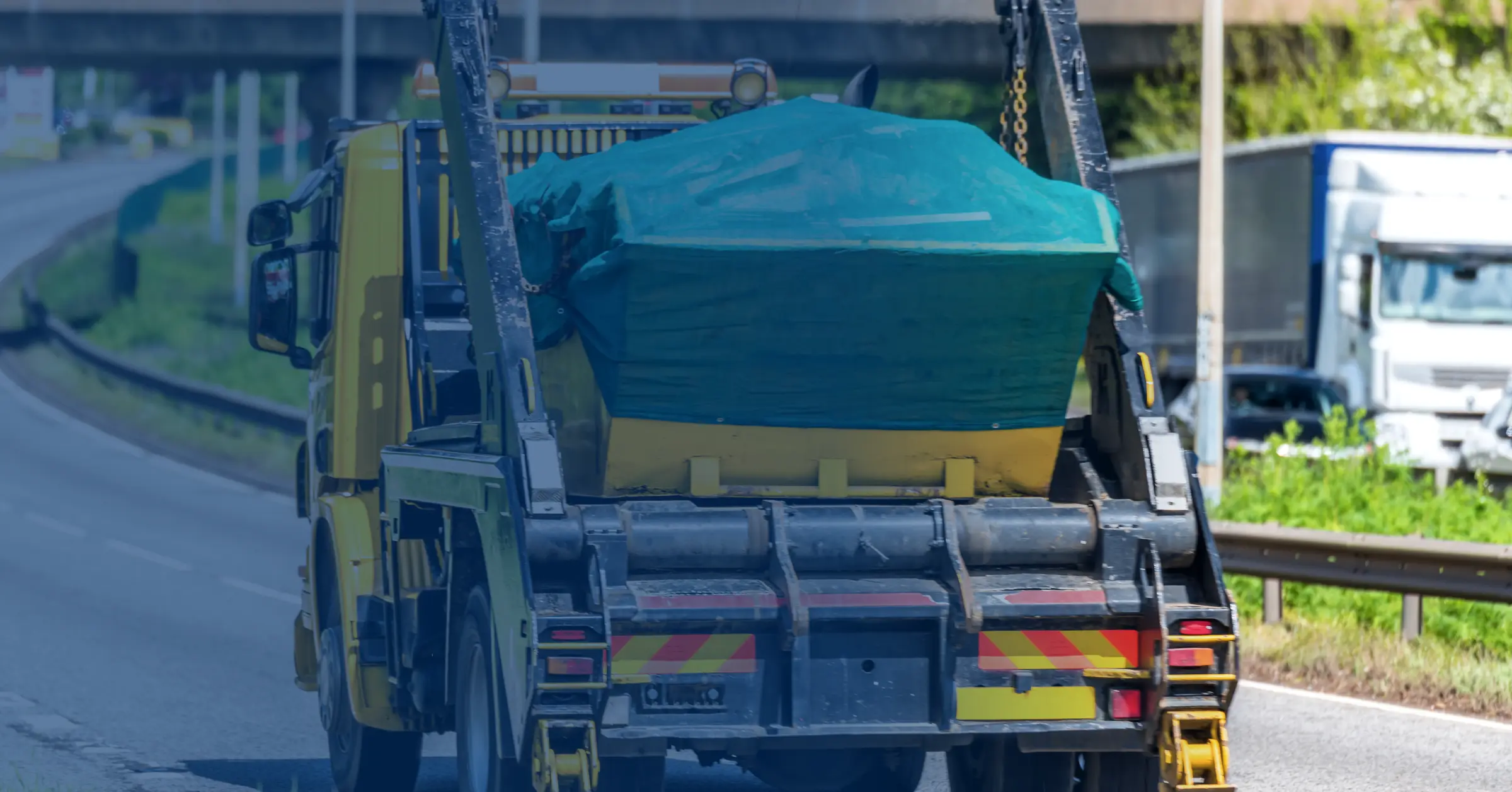 A skip lorry carrying a sheeted skip along a dual carriageway
