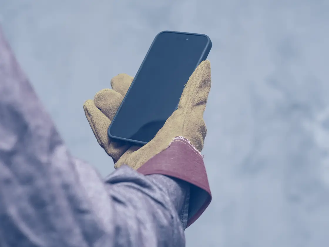 A work-gloved hand holding a phone at the kerbside