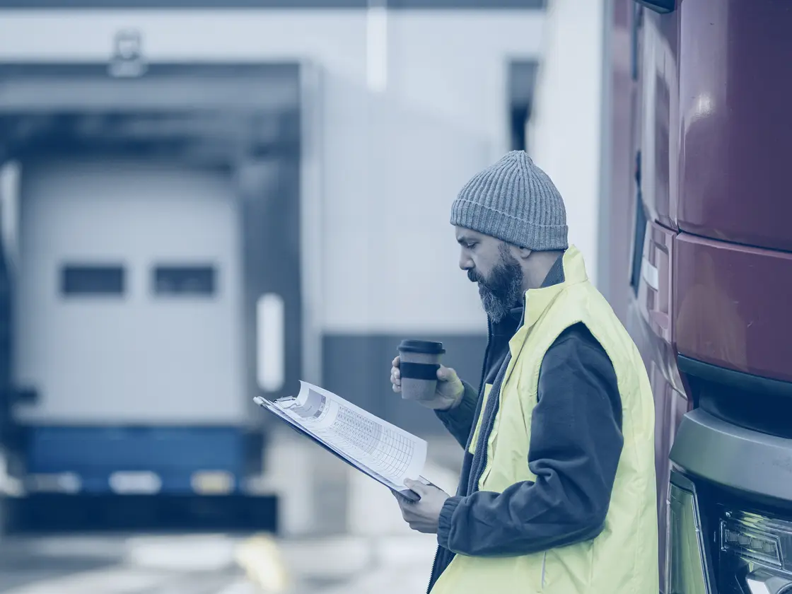 A driver working through delivery paperwork on a clipboard beside his lorry
