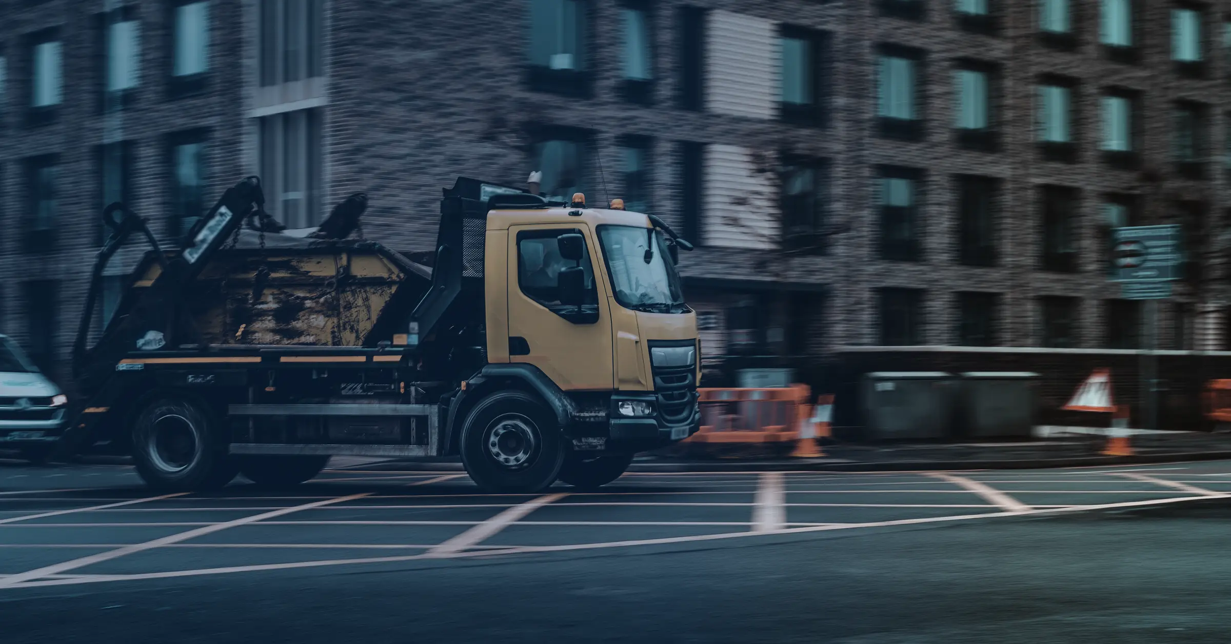 A skip lorry carrying a loaded skip through a city street